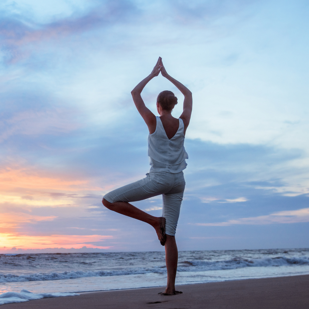 Women doing tree pose on a beach